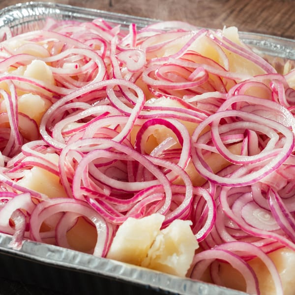 Close-up of boiled yuca pieces topped with thinly sliced red onions in a foil container.