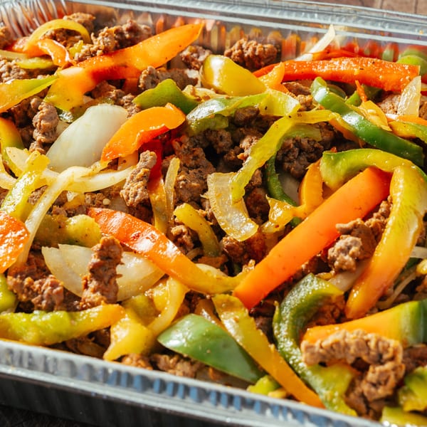 Close-up of Dominican-style beef with colorful bell peppers and onions in a foil tray.