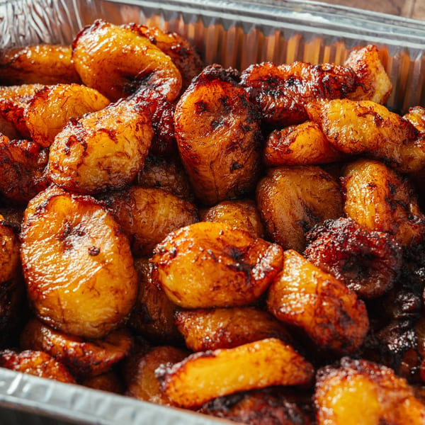 Close-up of golden-brown, caramelized sweet plantains (maduros) in a silver foil container.