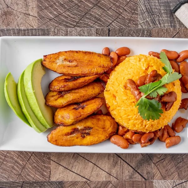 Dominican dish with yellow rice, red beans, fried plantains, and sliced avocado on a white plate.