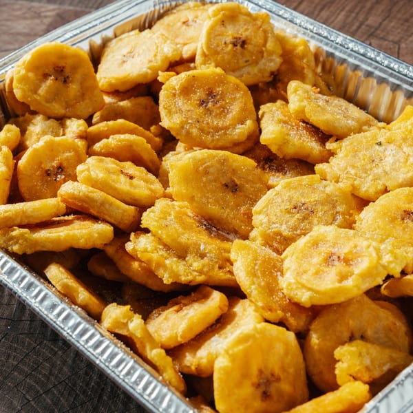 Close-up of golden-fried tostones, or plantain slices, in a silver foil container.