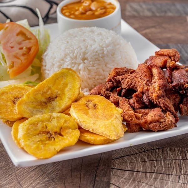 Dominican fried chicken with rice, plantains, salad, and a side of beans on a white plate.