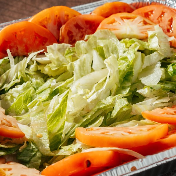 Close-up of a fresh salad with sliced tomatoes and shredded lettuce in a foil container.