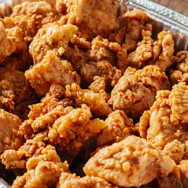 Close-up of crispy fried chicken pieces, a popular Dominican dish, in a foil container.
