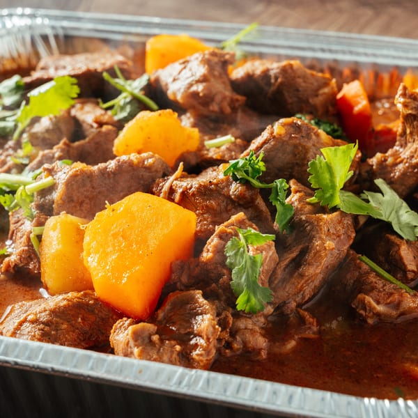 Close-up of Dominican stewed beef with potatoes and cilantro in a foil container.