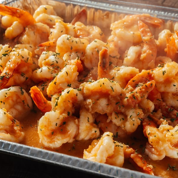 Steaming Dominican shrimp in a rich orange sauce, garnished with green herbs, in a foil pan.