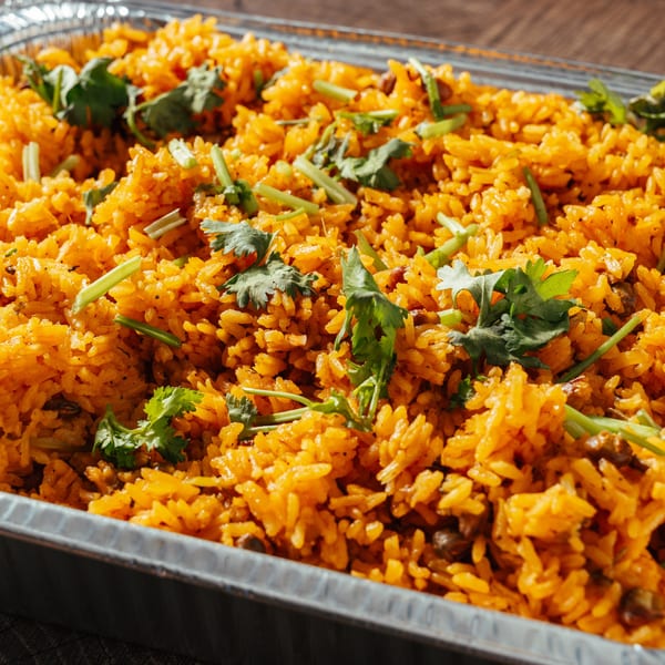 Close-up of vibrant yellow Dominican rice with green herbs in a foil tray.