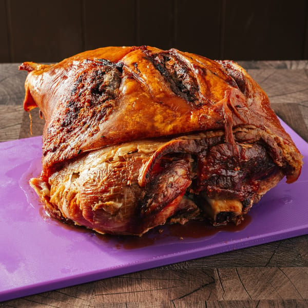 Crispy, golden-brown roasted pork shoulder, pernil, on a purple cutting board, ready to be carved.