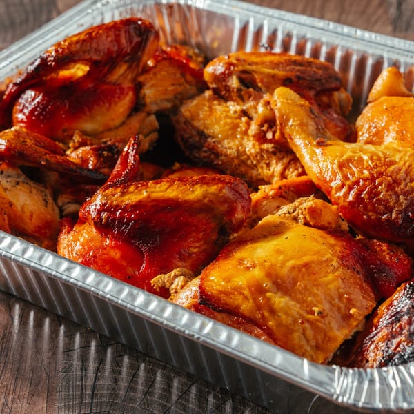 Close-up of golden-brown roasted chicken pieces in a silver foil pan on a wooden table.